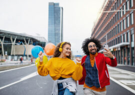 Portrait of young couple with smartphone making video outdoors on street, tik tok concept.