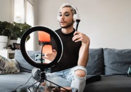 Gay man streaming online make up video tutorial with mobile phone indoors at home - Lgbt, drag queen, technology trendy concept - Focus in face