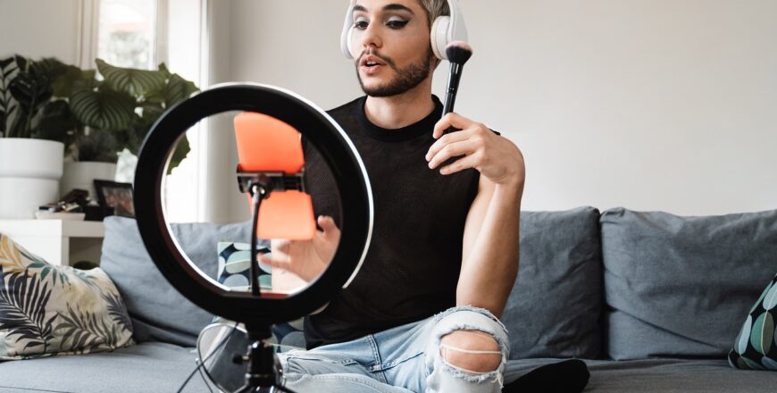 Gay man streaming online make up video tutorial with mobile phone indoors at home - Lgbt, drag queen, technology trendy concept - Focus in face