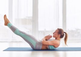 Young woman practicing yoga asana Ardha Navasana exercise at the bright yoga class with large windows