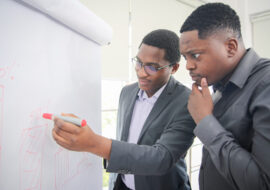 African American young man writing note on a transparent wipe board and thinking of a solution for him work-related problems, Colleagues Having A Business Meeting