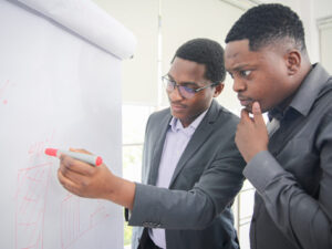 African American young man writing note on a transparent wipe board and thinking of a solution for him work-related problems, Colleagues Having A Business Meeting