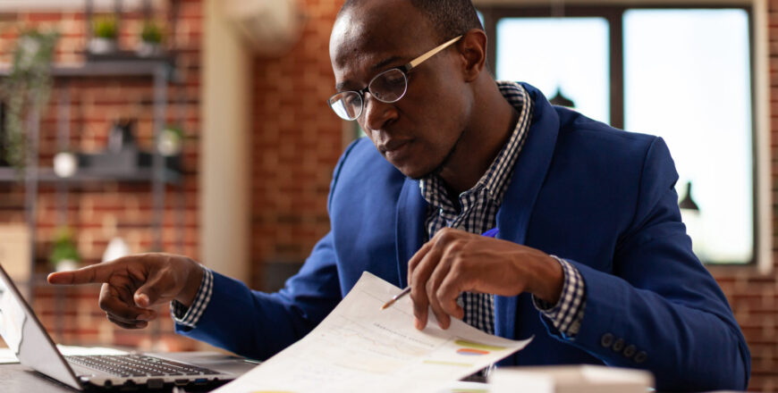 Business man analyzing papers on clipboard to plan marketing strategy with laptop