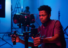 Young African American camera operator shooting on professional camera in dark studio