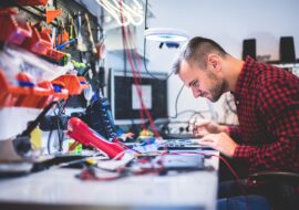 Side view of young concentrated guy repairing laptop and sitting at table between different gadgets and tools