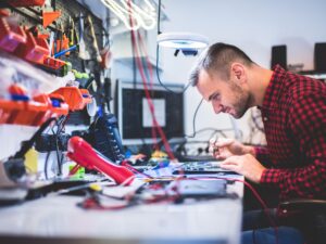 Side view of young concentrated guy repairing laptop and sitting at table between different gadgets and tools