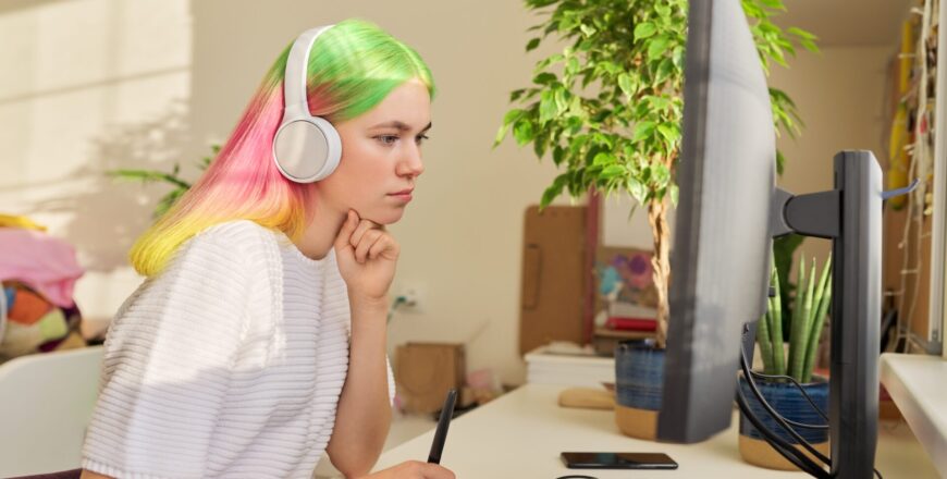 Girl teenager artist in headphones drawing on computer using graphics tablet